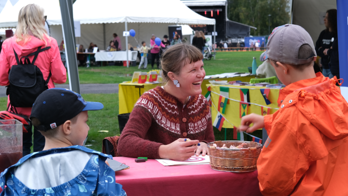 Oulu kylässä -festivaalin esittelypiste, edustalla kaksi lasta ja esittelypisteellä hymyilevä henkilö