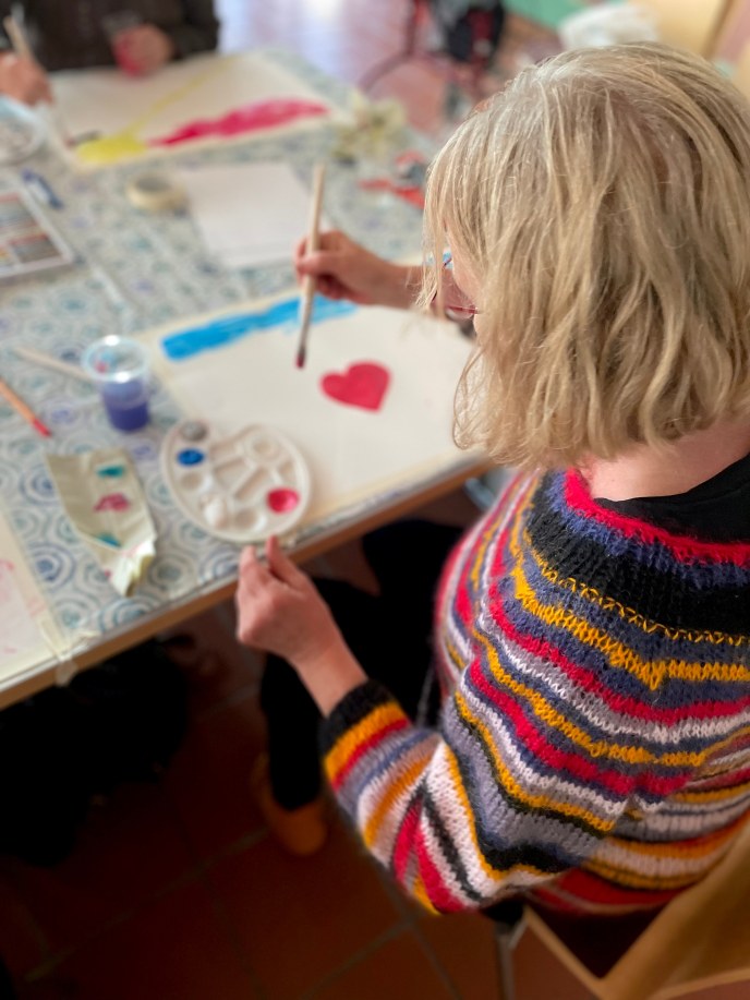 Henkilö maalaa vesiväreillä, paperille on maalattu sydän.