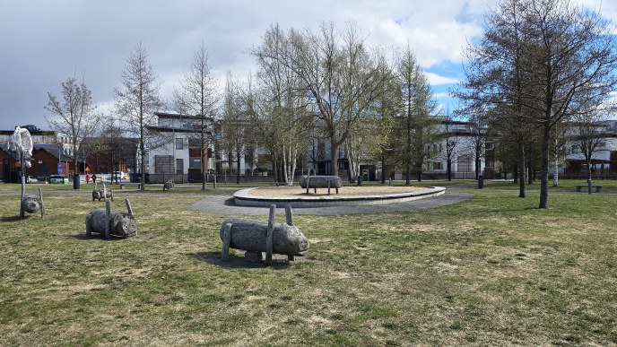 Kuvassa vihreä nurmialue, jossa puisia porsaspatsaita