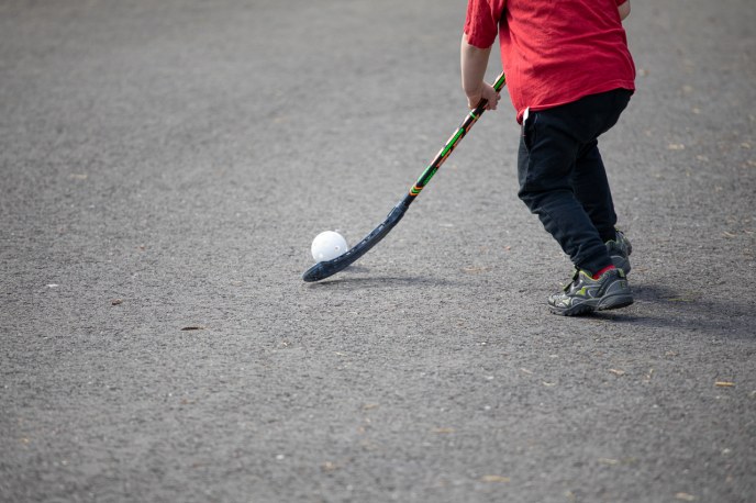 pieni lapsi pelaa salibandya asfaltilla