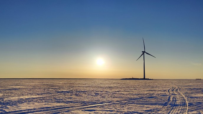 Kuvassa on talvisella merellä auringon laskun aikaan kuvattu tuulimylly.