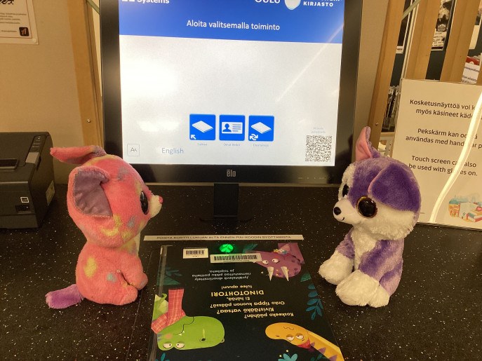 Pehmoketut kirjastoautomaatilla lainaamassa kirjaa