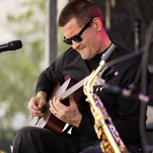 Mies soittaa kitaraa, edustalla saksofoni ja mikki