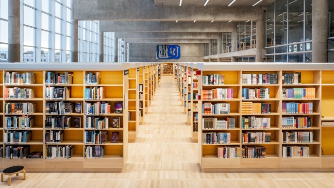 Suuri, korkea kirjastosali, peräkkäisiä kirjahyllyjä, joiden välissä käytävä.