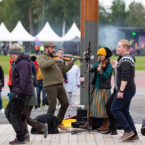 Two people playing violin and people dancing in front of them